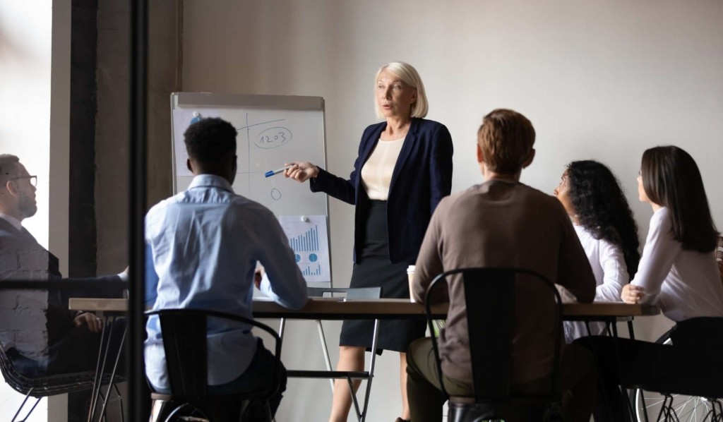 A trainer presenting at a whiteboard to a seated group of colleagues during a corporate workshop.