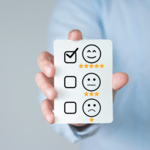 A person holding a white card featuring a customer feedback survey with a checkmark next to a happy smiley face rating with five yellow stars.