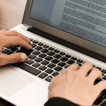 A close-up view of a person's hands typing on a laptop keyboard with a detailed document open on the screen.
